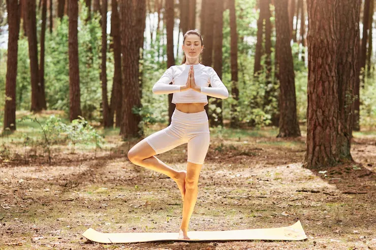 Person performing vrksasana tree pose in a peaceful outdoor yoga setting